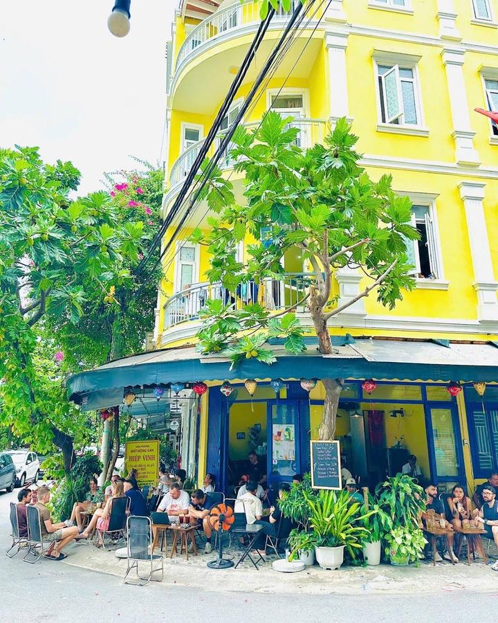 The yellow corner building of Góc Nhỏ Cà Phê on An Thượng, with a tall leafy tree out front and customers seated at tables under the awning